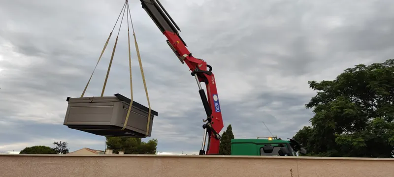 Spa tenu à l'horizontale par une grue articulée rouge, au-dessus d'une clôture verte