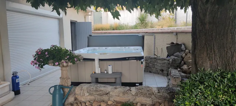 Spa blanc installé sur la terrasse, une fleur rose au premier plan, l'accès au jardin