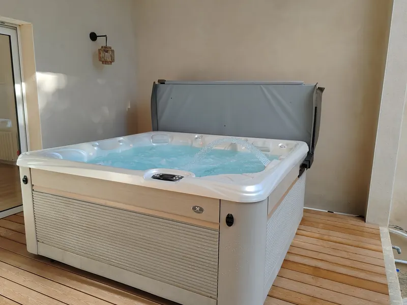 Spa en eau vu d'un autre angle, couverture relevée, terrasse en bois et mur beige