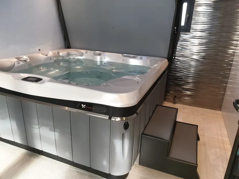 Spa Caldera rempli, couvercle relevé, avec marchepied dans une pièce intérieure carrelée à Frontignan