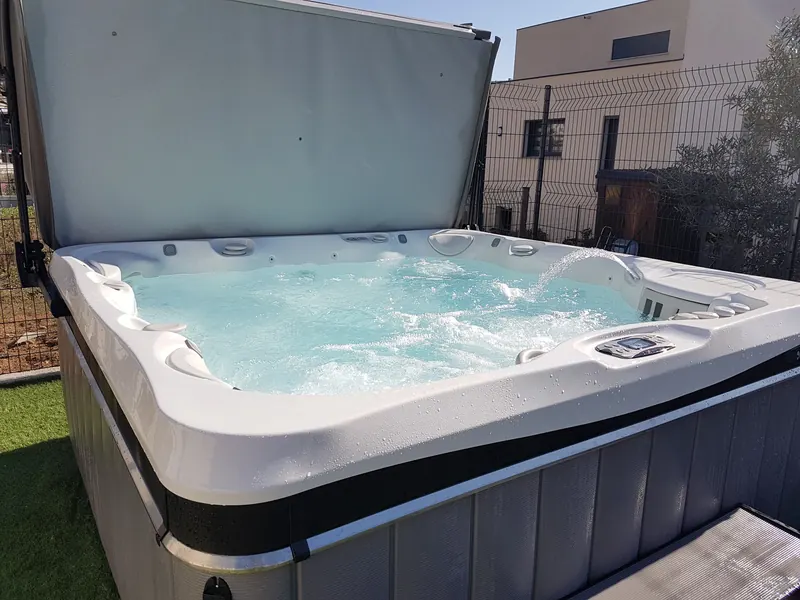 Cuve du spa remplie, jets et cascade en marche, couverture relevée, dans un jardin à Agde