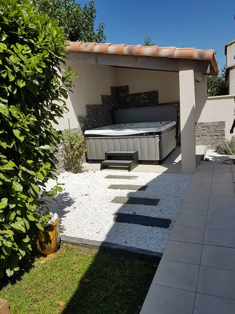 Allée de pas en pierre sur gravier blanc menant à un abri à toit de tuiles, au fond du jardin