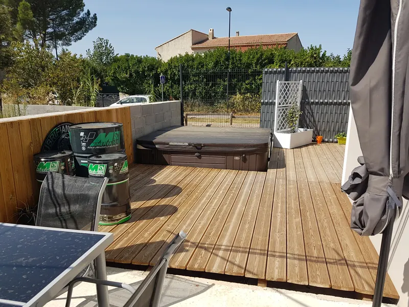 Spa à couverture brune logé dans une terrasse en bois, vu depuis la table de jardin, à Gignac