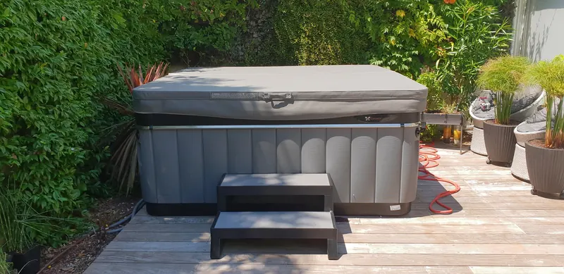 Spa gris couvert, avec marchepied, sur une terrasse en bois contre une haie à La Grande-Motte