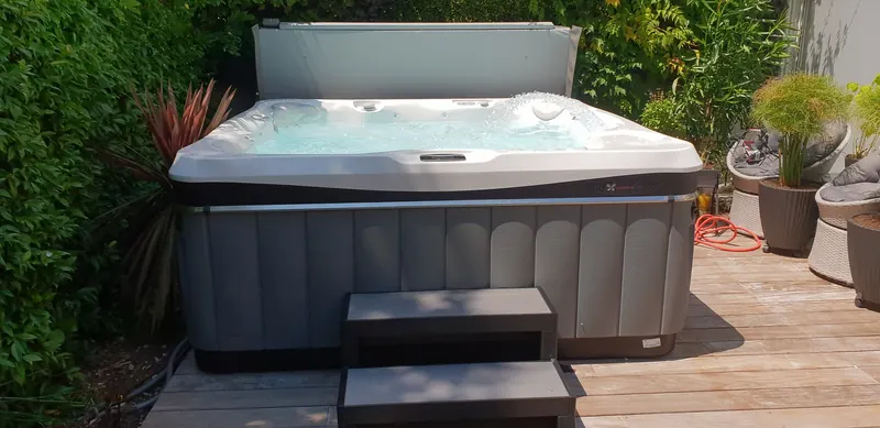 Spa Caldera ouvert, eau en mouvement, couverture relevée à l'arrière, sur une terrasse en bois à La Grande-Motte