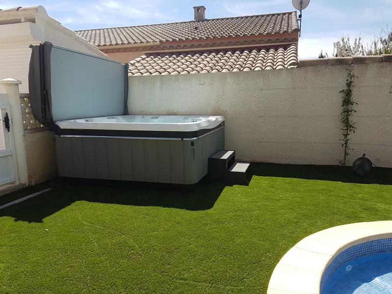 Spa gris couvercle relevé, avec marchepied, contre le mur du jardin à Maureilhan