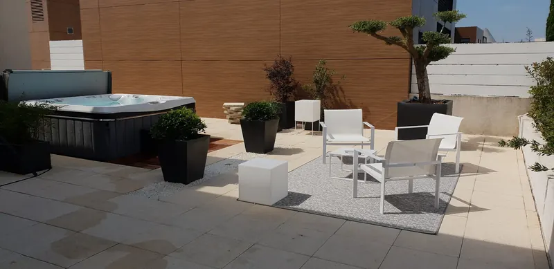 Toit-terrasse à Montpellier avec le spa au fond, des bacs plantés et un salon de jardin blanc