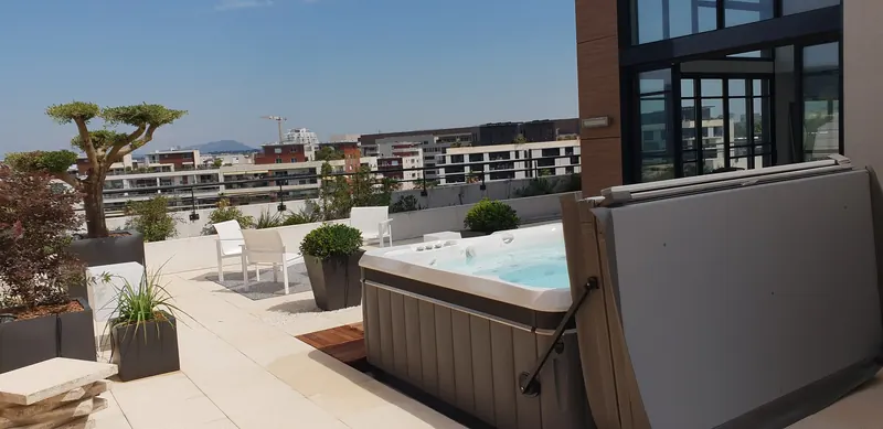 Spa Caldera rempli sur un toit-terrasse à Montpellier, couverture relevée, vue sur les immeubles voisins