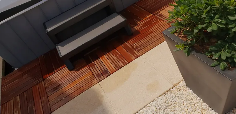 Marchepied gris du spa posé sur des caillebotis en bois, à côté d'un bac planté