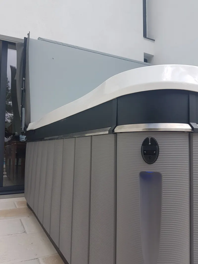 Angle d'un spa à habillage gris et liseré inox, couverture relevée contre la façade, à Saint-Clément-de-Rivière