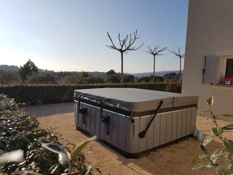 Spa gris avec lève-couverture au pied d'une maison, entre les haies, face aux collines à Saint-Pierre-de-Vassols