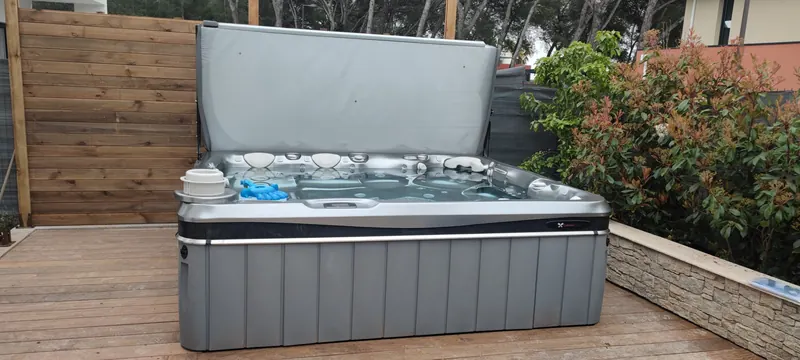 Spa gris à couverture relevée sur une terrasse en bois, palissade, muret de pierre et haie