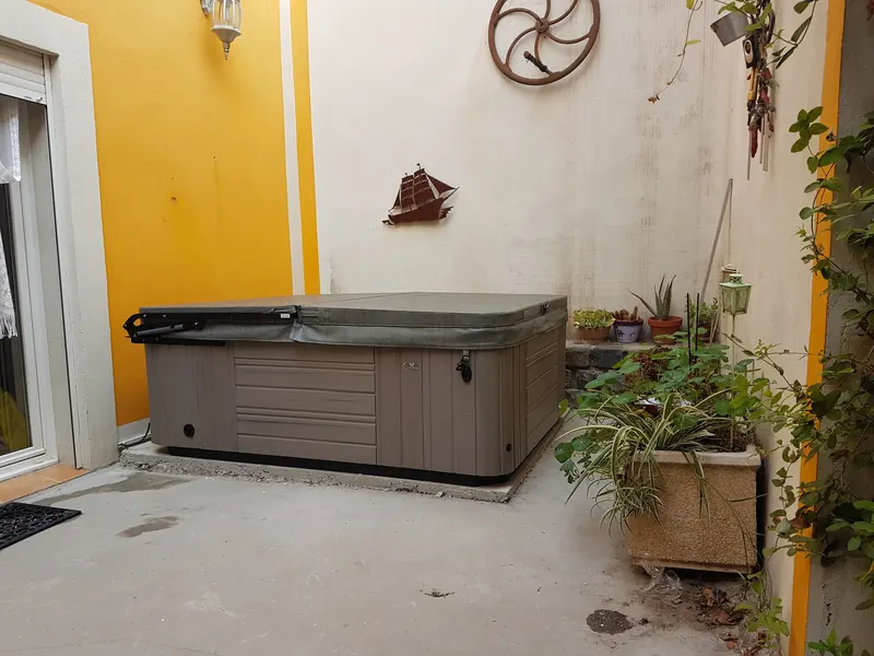 Spa Caldera couvert, habillage gris, posé sur une dalle béton dans une cour aux murs jaune et crème à Bessan