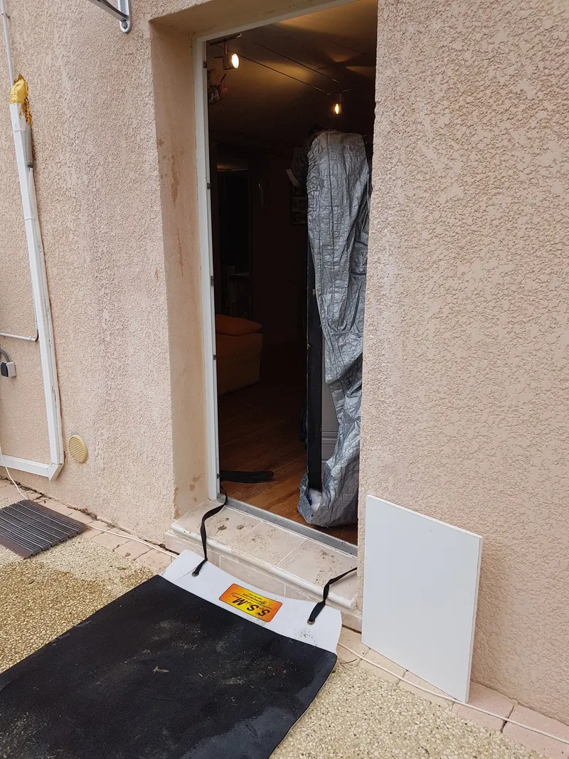 Spa emballé, dressé sur la tranche, qui passe la porte d'une maison, un tapis de glissement posé au seuil