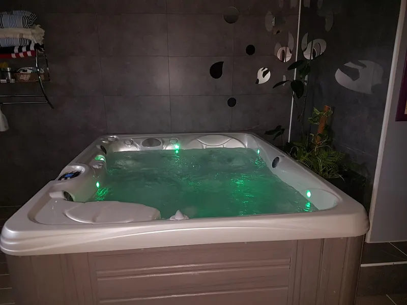 Spa Caldera Kauai en marche, jets actifs et éclairage vert, contre un mur carrelé gris