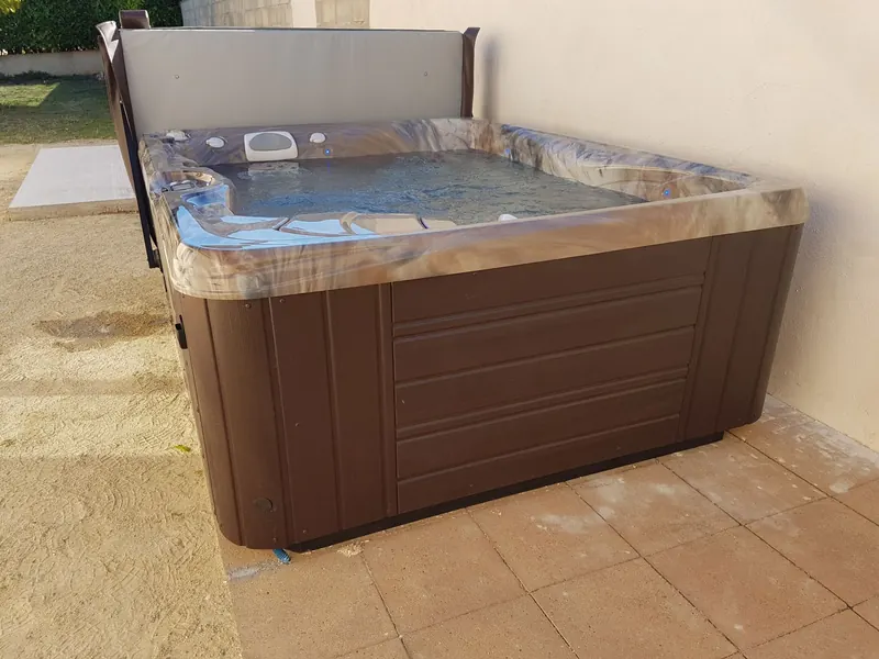 Cuve du spa remplie d'eau, margelle en acrylique marbré et habillage brun, à Mèze