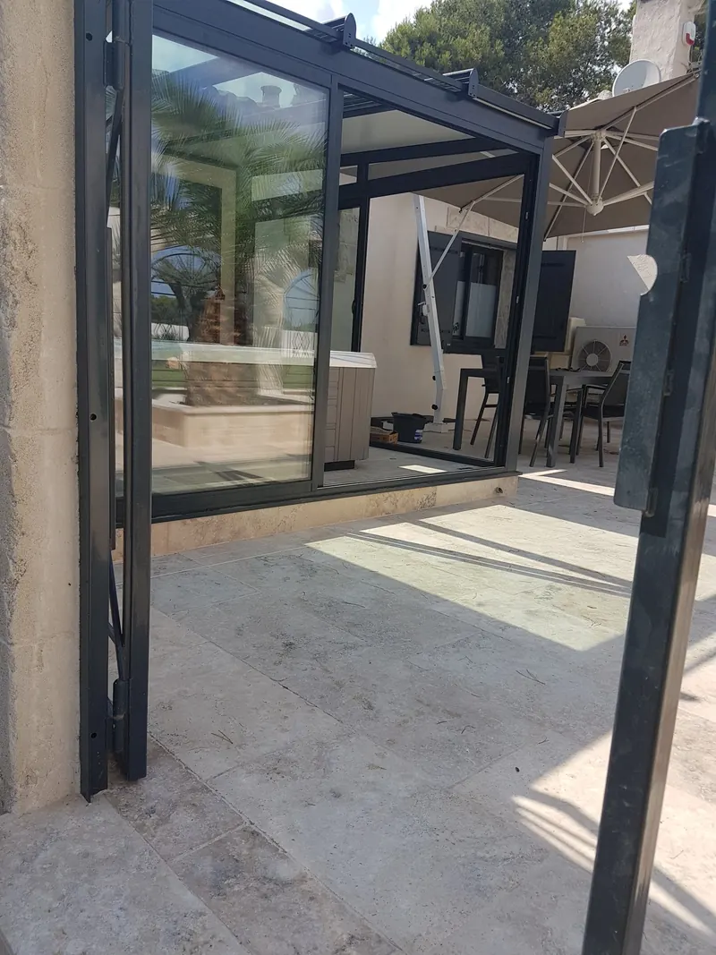 Véranda vitrée à cadre anthracite abritant un spa, vue depuis le portillon