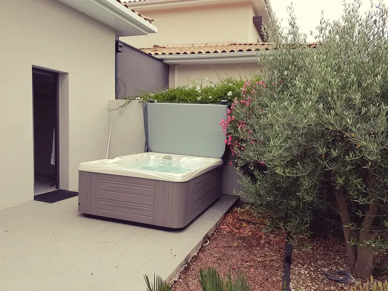 Spa sur une terrasse carrelée près d'une porte de maison, entre un muret et un olivier, à Teyran