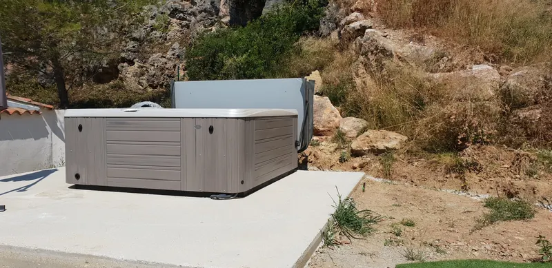 Spa à habillage gris vu de face sur sa dalle béton, couverture relevée sur le lève-couverture, à Poussan