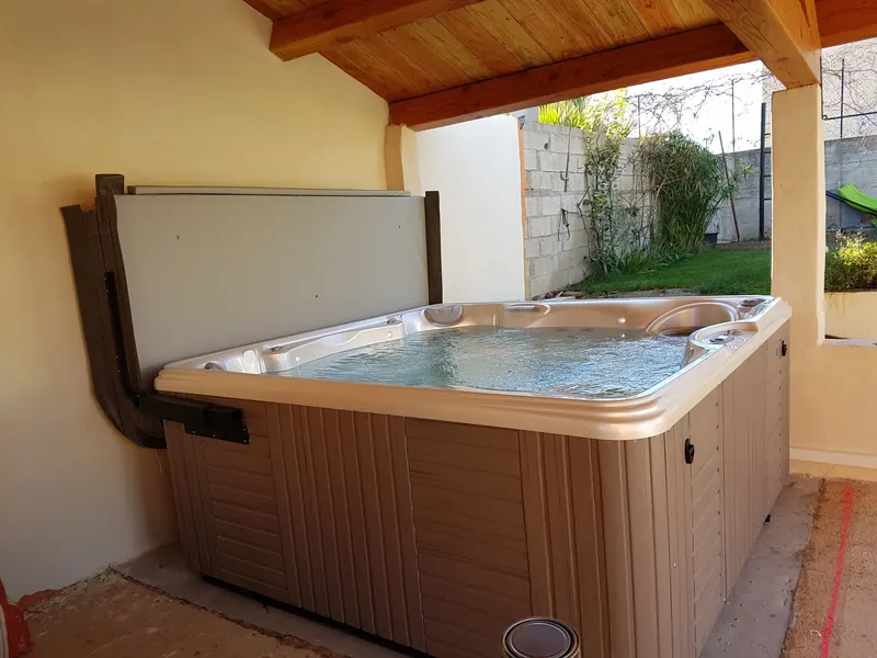 Spa Caldera Marino rempli sous une pergola en bois, lève-couverture fixé au mur, jardin en arrière-plan