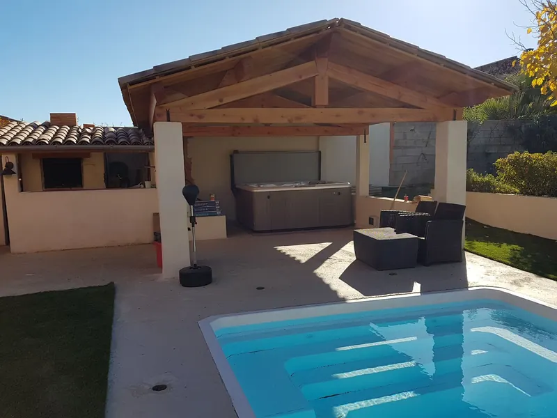 Pergola en bois abritant le spa, salon de jardin et piscine au premier plan à Cazouls-lès-Béziers