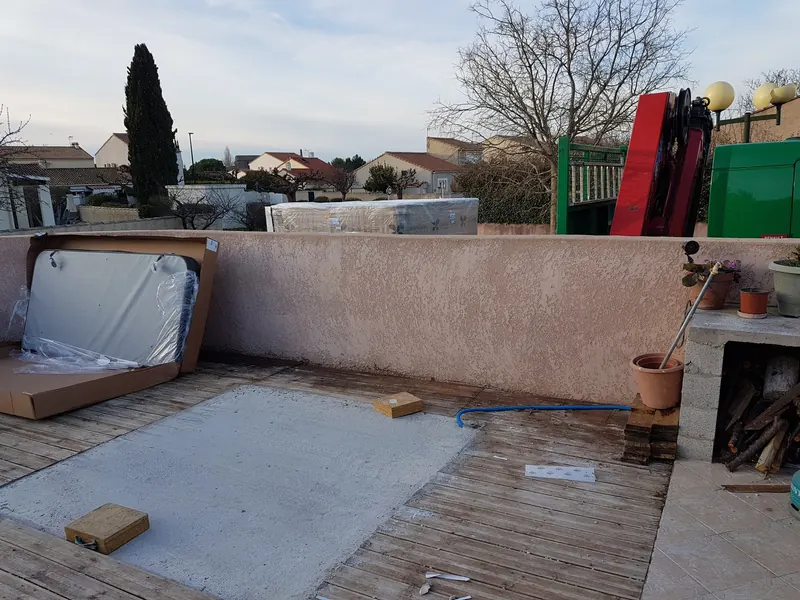 Dalle béton préparée dans une terrasse en bois, spa emballé et camion-grue derrière le mur à Loupian