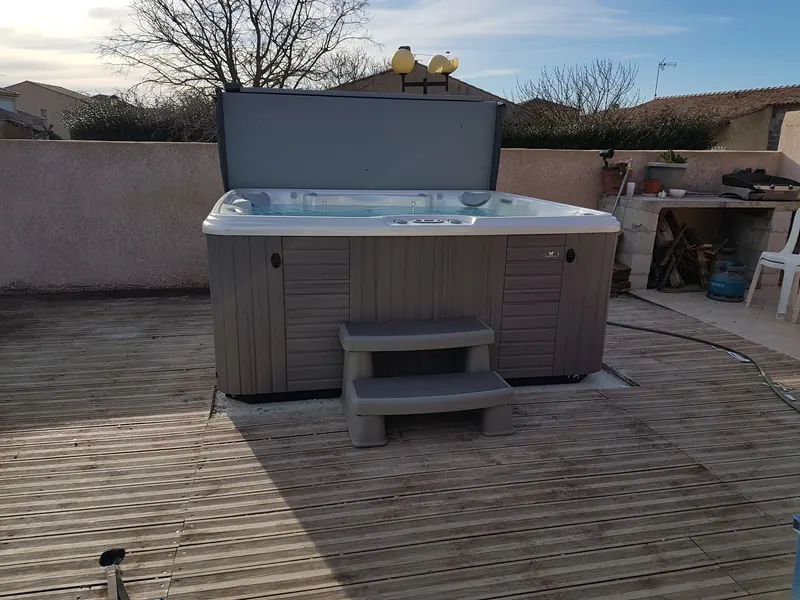 Spa Caldera gris en eau posé sur une terrasse en bois, couverture relevée et marchepied, à Loupian