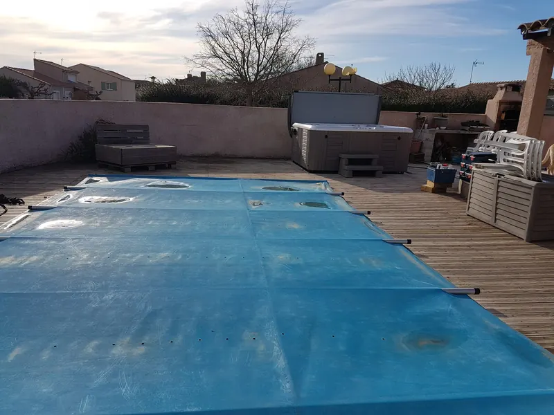 Terrasse en bois avec piscine bâchée et spa installé contre le mur du fond à Loupian