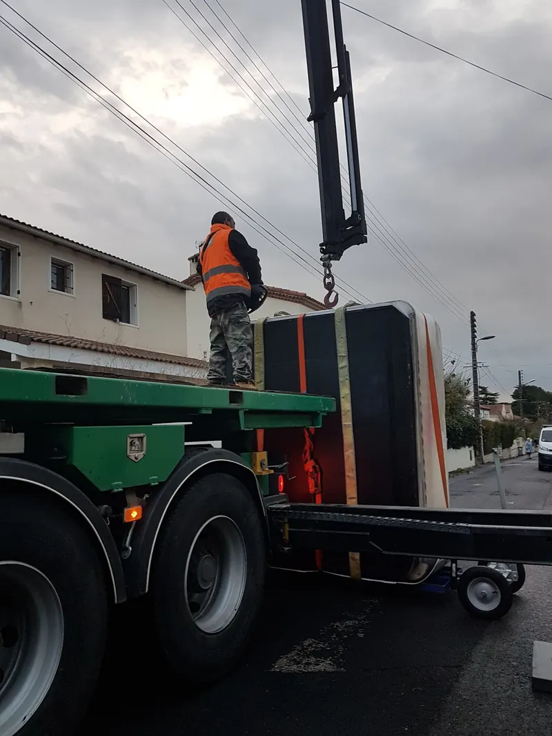 Spa emballé dressé sur un chariot, sous le crochet d'un camion-grue, dans une rue de Castelnau-le-Lez