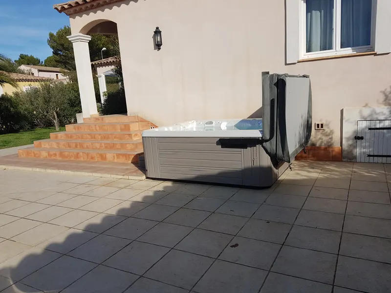 Spa installé contre la façade d'une maison, au pied d'un escalier en terre cuite, lève-couvercle replié