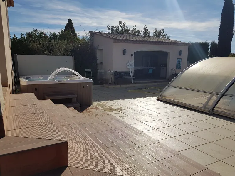 Vue de la terrasse : spa en marche contre la maison, pool-house et piscine sous abri