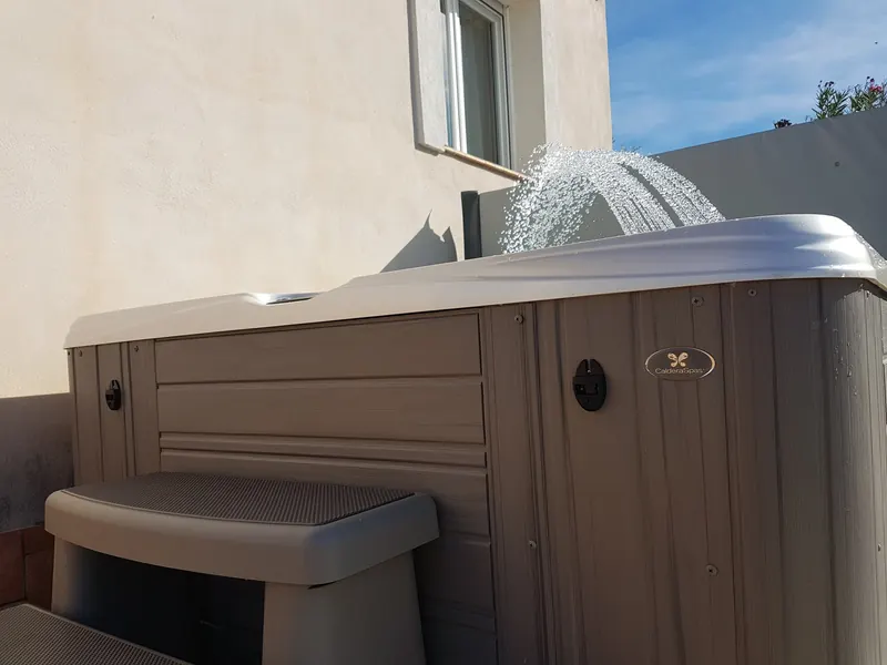Habillage gris du spa avec le logo Caldera Spas et marchepied, fontaine en marche