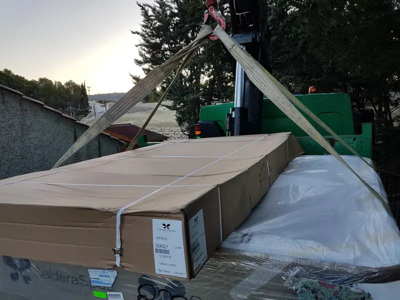 Carton Caldera Spas étiqueté Martinique sanglé sur le plateau d'un camion-grue à Gigean