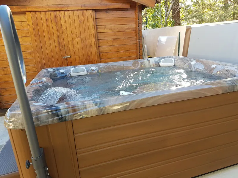 Spa à coque marbrée en marche, cascade et jets, devant un abri de jardin en bois à Gigean