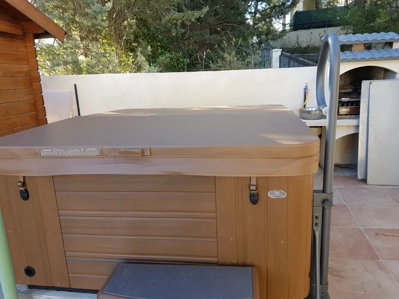 Spa Caldera fermé par sa couverture brune, avec marchepied et rampe, sur une terrasse à Gigean