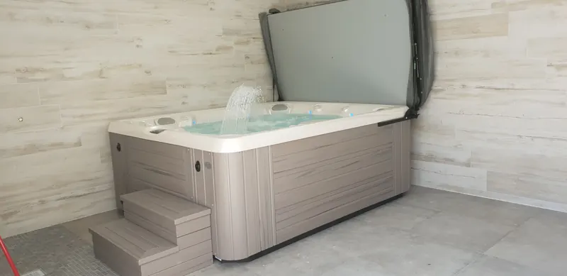 Spa à habillage gris taupe, couverture relevée et marchepied assorti, dans la pièce intérieure