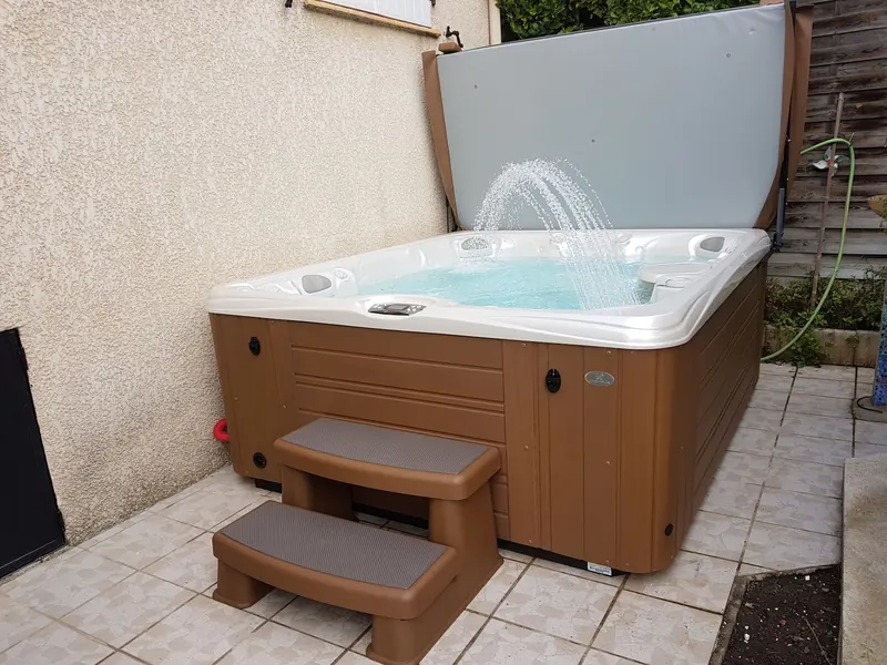 Spa Caldera Martinique rempli, fontaine en marche et couvercle relevé, sur une terrasse carrelée à Pignan