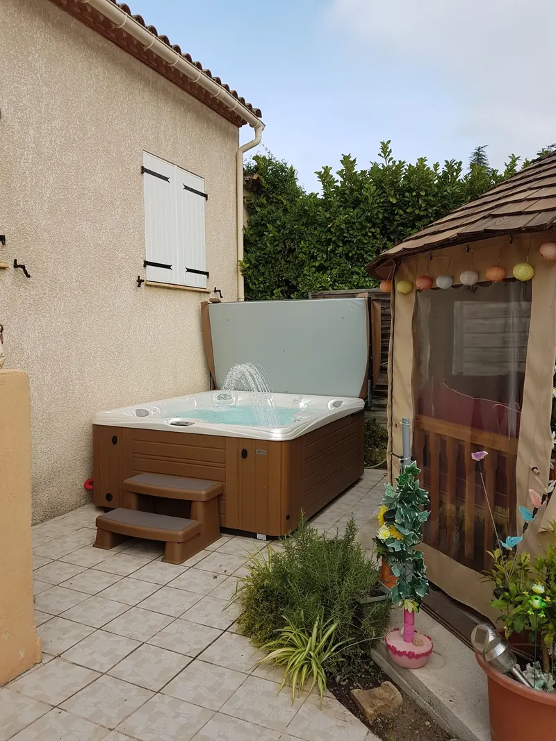 Spa ouvert au fond d'une terrasse carrelée, entre la maison et une tonnelle, à Pignan