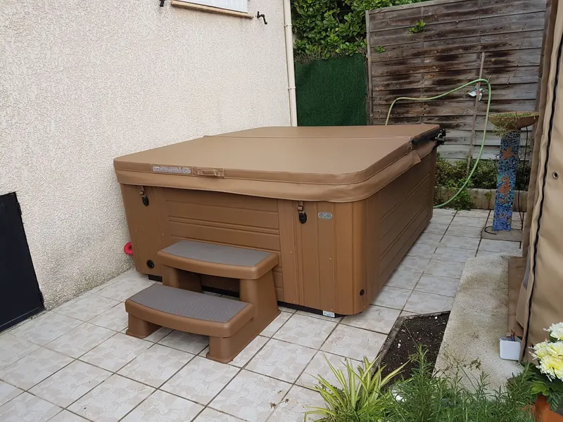 Spa à habillage brun fermé par sa couverture, avec son marchepied, contre le mur de la maison à Pignan