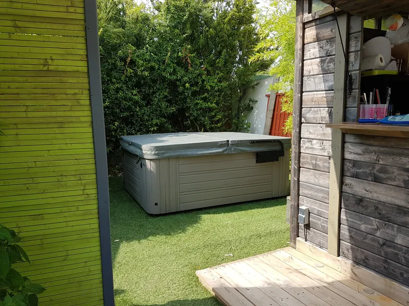 Spa sous sa couverture grise sur du gazon synthétique, vu depuis la terrasse d'un abri en bois à Poussan