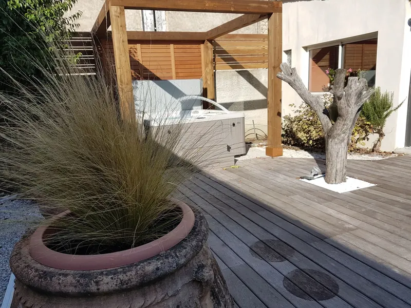 Spa sous sa pergola en bois, derrière une jarre plantée de graminées sur la terrasse