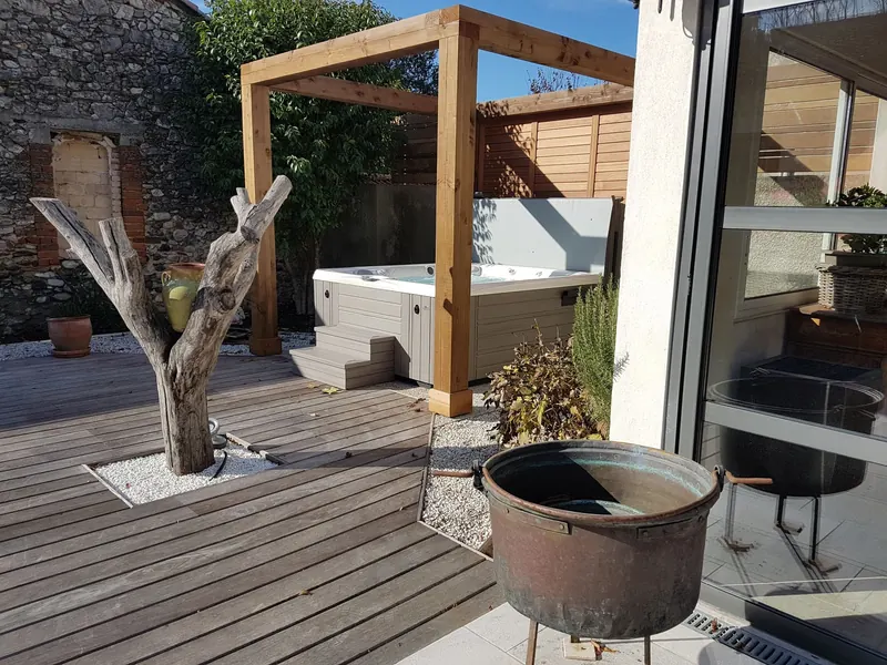 Spa ouvert sous la pergola, au fond de la terrasse en bois, près d'un tronc d'arbre décoratif