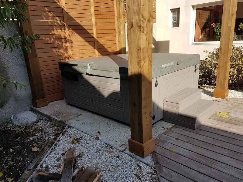 Couvercle fermé sur le spa posé sur sa dalle sous la pergola, marchepied sur la terrasse en bois