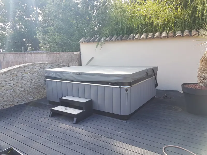 Spa Caldera gris installé sur une terrasse en lames, contre un mur crépi, avec son marchepied, à Mèze