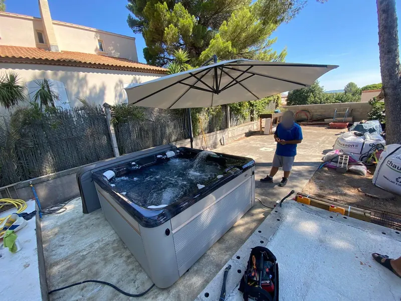 Spa noir et blanc sous le parasol, dans un jardin clos par une clôture en bois