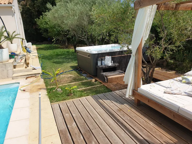 Spa en place près de la terrasse en bois, marche et accessoires posés devant, carton au pied