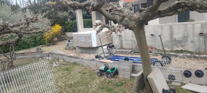 Jardin avec le spa emballé sur sa dalle, chariot bleu, dalles et supports ronds au sol