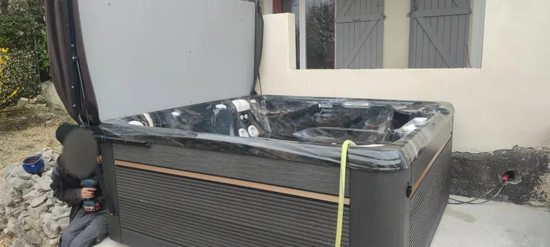 Spa déballé sur la dalle béton, couverture relevée, personne accroupie avec une visseuse