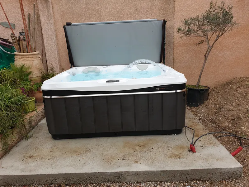 Spa Caldera Spas rempli, couverture relevée, posé sur une dalle béton contre un mur à Sète