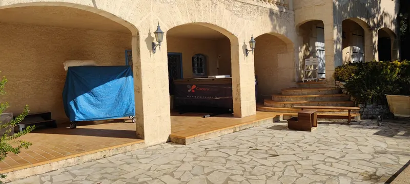 Spa emballé sous une arcade de villa en pierre, bâche bleue sur roulettes dans l'arcade voisine